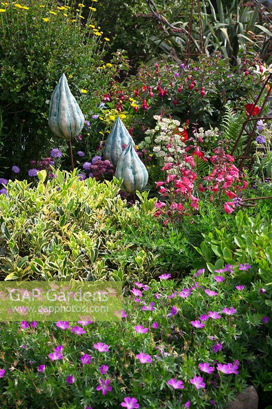 Decorative pottery seedheads among Euonymus, pink Geraniums, Penstemon 'Garnet Red', Fuschia 'Empress of Prussia' and Astrantia.