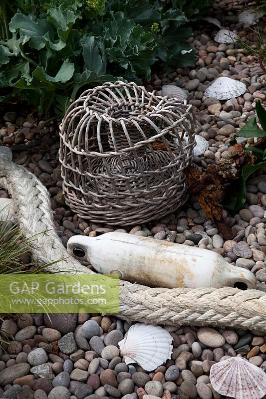 Woven lobster pot, fishing float and maritime rope with Crambe maritima - Sea Kale,  pebbles and shells.