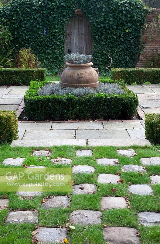 Grass and stone setts form a chequered path to pergola covered small Buxus - box edged, Lavender filled knot garden with terracotta urn - Brightling Down Farm