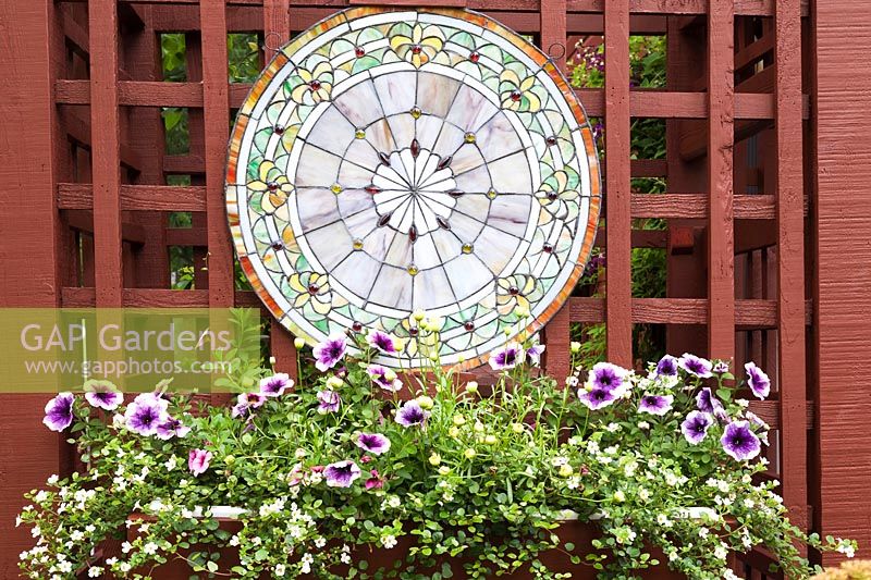 Purple Petunia 'Night Sky', Calibrachoa, Lobelia, yellow Sanvitalia and Creeping zinnia flowers in wooden flower box with decorative round stained glass window in summer, Quebec, Canada