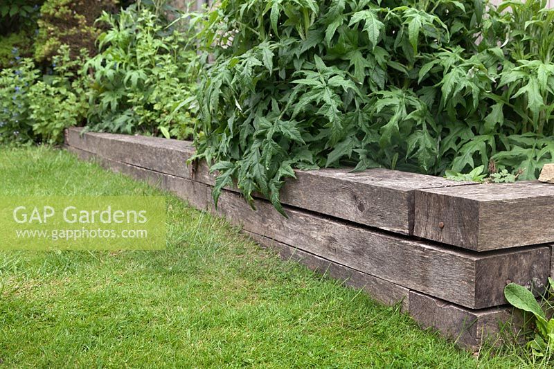 Corner detail of raised bed on sloping lawn made from timber showing increase in height