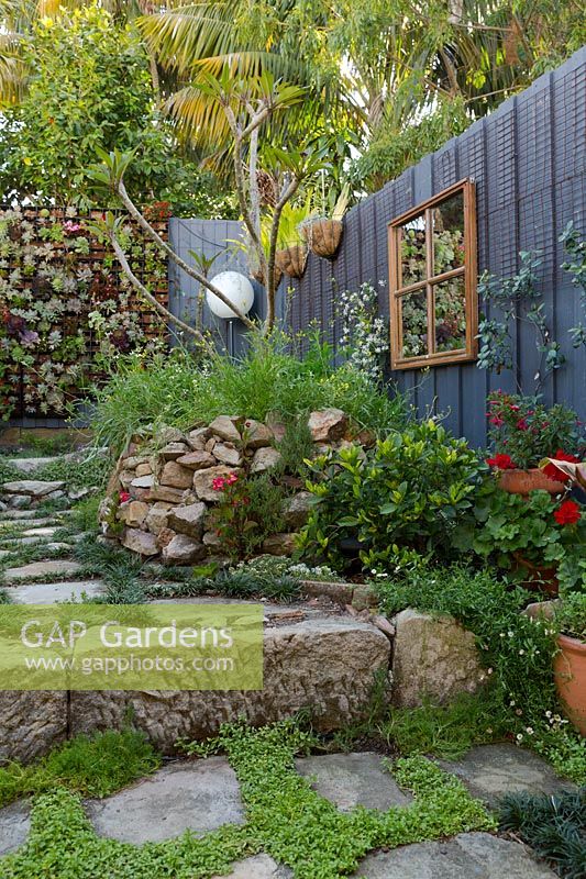 Inner city courtyard garden with framed mirror, sandstone raised bed and various plantings