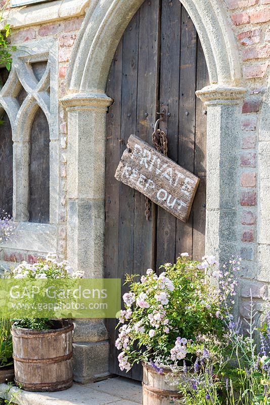 A Gothic entrance flanked by recycled wooden barrels planted with roses.