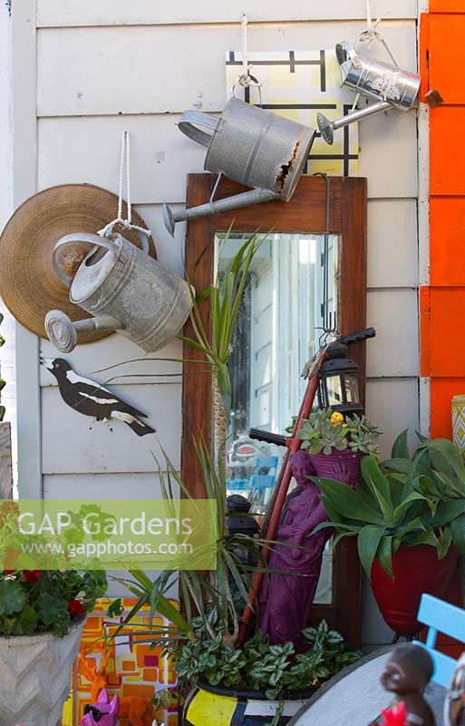 Front verandah detail with a collection of eclectic objects featuring three old metal watering cans, a mirrored wardrobe door and a cut out metal magpie.