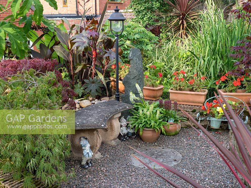 A gravel patio in front of a stone Bench with range of tropical planting including Canna's, Acer and Ricinus communis.