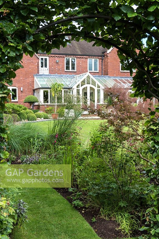 Glimpse of the Renwick's modern home, seen through an arch cut into a hornbeam hedge.