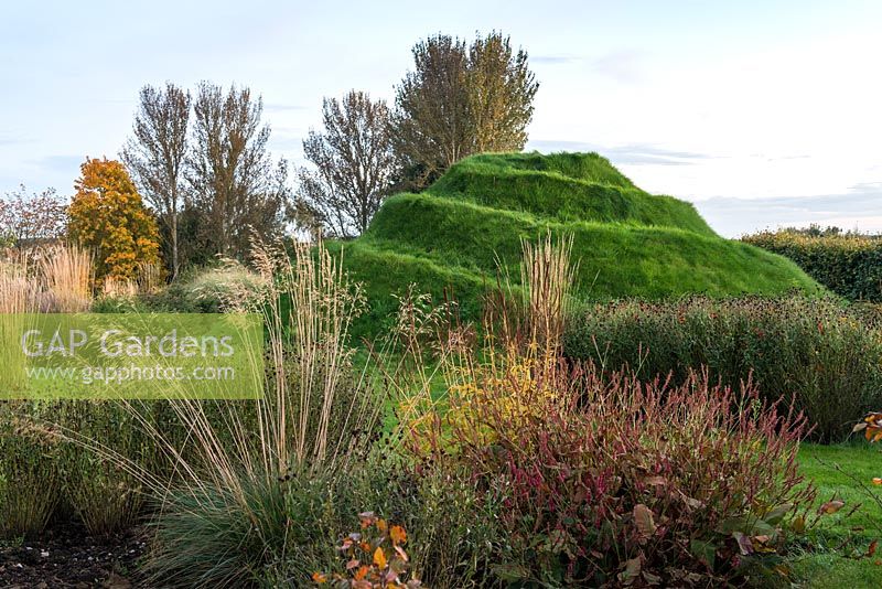 Mound, a grassy viewing platform, seen through beds of ornamental grasses and perennials.