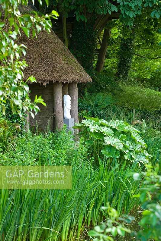 Woodland garden with thatched summerhouse and modern sculpture - Asthall Manor, Oxfordshire