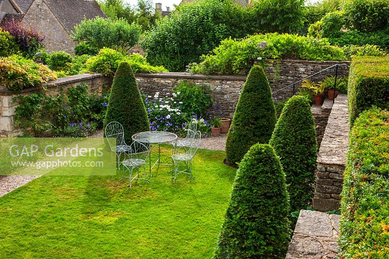 Yew cones on lawn with table and chairs, Burford, Oxfordshire.