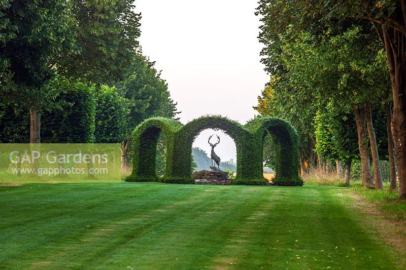 Lawn and avenue of Tilia platyphyllos 'Rubra' with central yew Rondel enclosing bronze stag sculpture