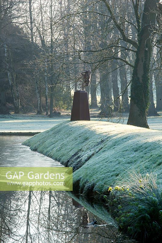 Figure head sculpture beside water and grassy bank

 