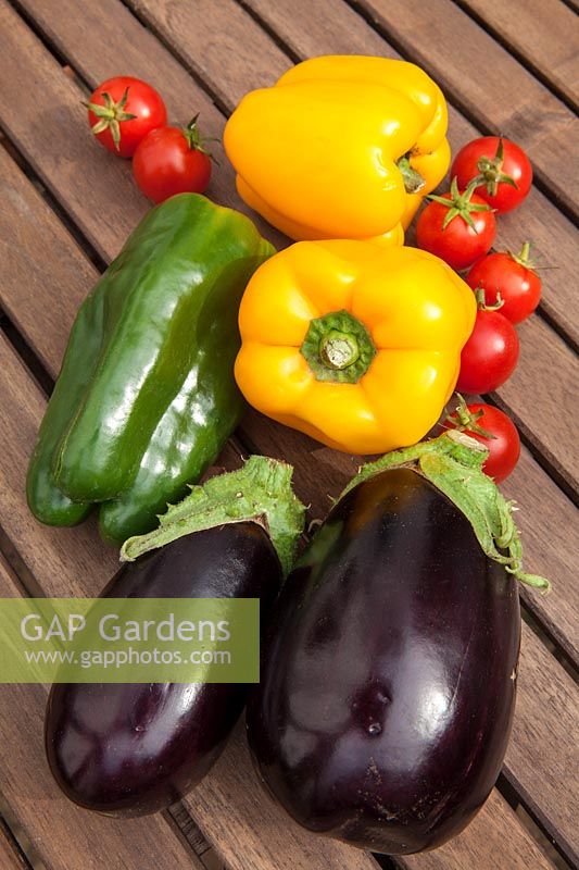 Colourful vegetables - Peppers, Tomatoes and Aubergines - outdoors on a wooden table