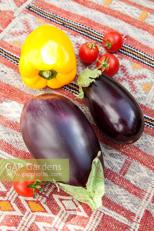Colourful fresh vegetables - Aubergines, yellow pepper and cherry tomatoes on a kilim covered table