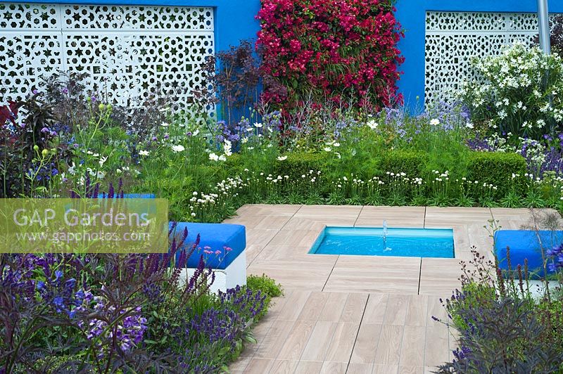 A blue and white themed Mediterranean style garden with cube seats, Bougainvillea and a small pool