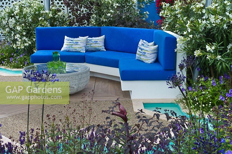 A paved seating area with cushions, Oleander and Agapanthus pools of water in a blue and white Mediterranean style garden