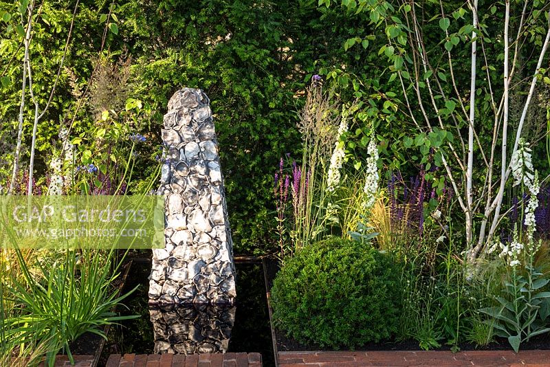 Contemporary garden with stone sculpture feature set in a rectangular pool of water