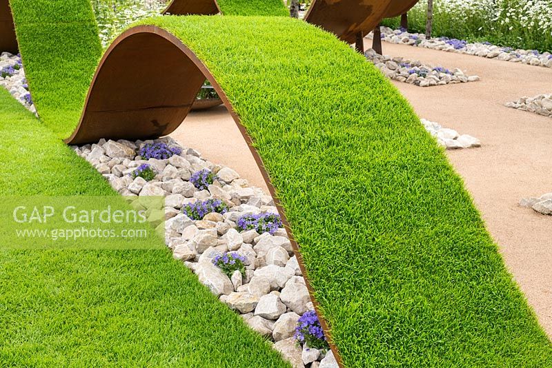Undulating waves of artificial turf, underplanted with Anemone blanda amongst stones. RHS Hampton Court Flower Show