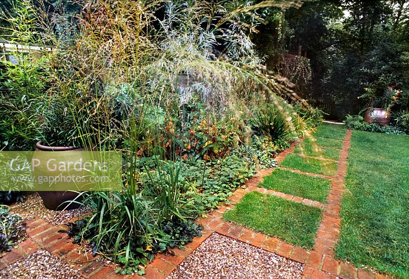 Shaded urban rear garden with lawn, paving, large urn & perennial border