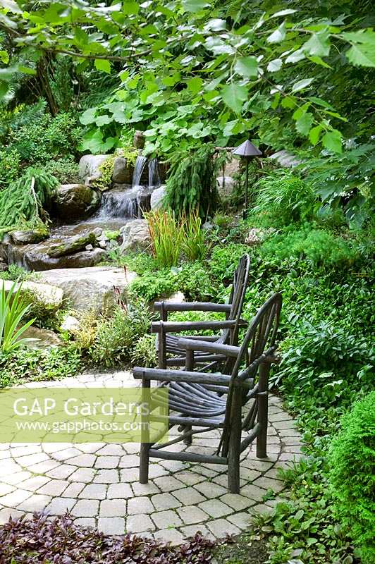 Garden scene with garden chairs, rock water fall, coniferes, shrubs and perennials