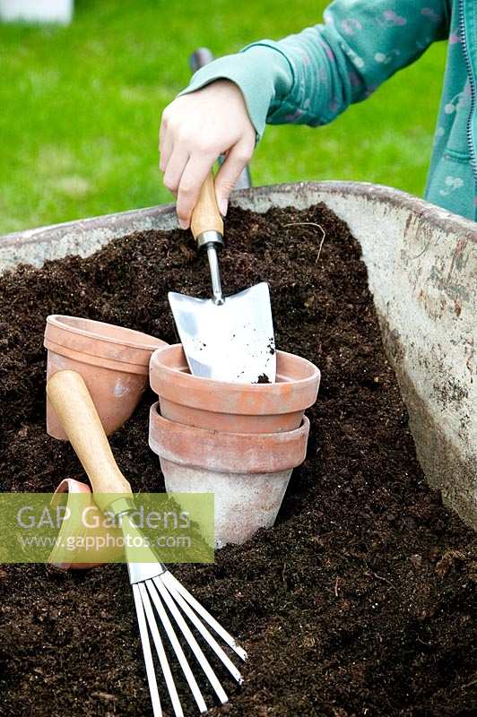 Clay pots and garden tools in potting soil, child is potting