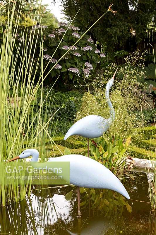 Bourton House Garden, Gloucestershire. Mid summer. Detail of the pond with statue of 'Two Herons' by Michael Lythgoe