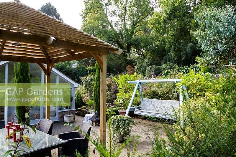 Jackie Healy's garden near Chepstow. Early autumn garden. Japanese style wooden 'pergola' and swing bench in the patio area