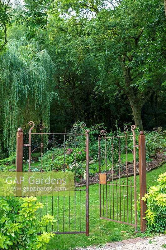 Jackie Healy's garden near Chepstow. Early autumn garden. Rustic metal gates lead to woodland garden