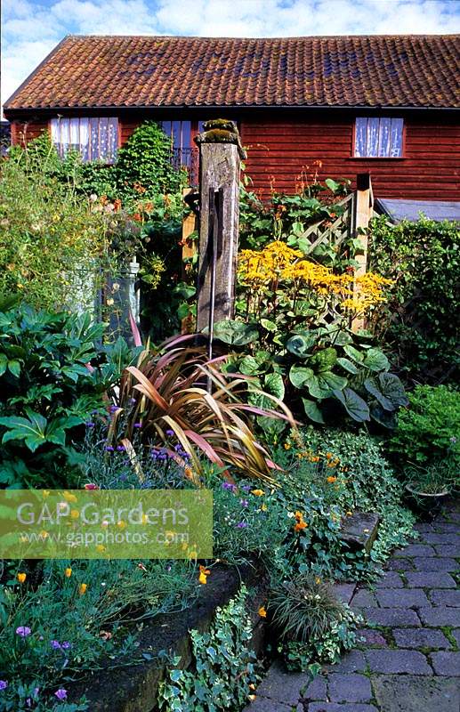 private garden Suffolk small courtyard garden with railway sleeper raised bed Phormium Ligularia runner beans