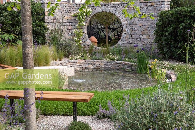 The Harmonious Garden of Life. An environmentally sustainable courtyard with a pond that is kept clean by the surrounding plants, encircled in clover to enrich the soil. A stone enclosure wall features a circular opening. Designer: Laurelie de la Salle. Sponsors: Mr and Mrs Cawthorn, Margheriti Piante.