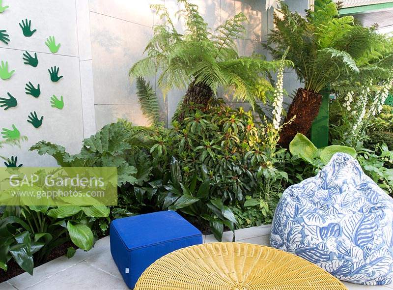 Modern and colourful living area with benches, tables and foliage planting. Designed by Kate Gould Gardens, sponsored by Greenfingers Charity, RHS Chelsea Flower Show, 2019.