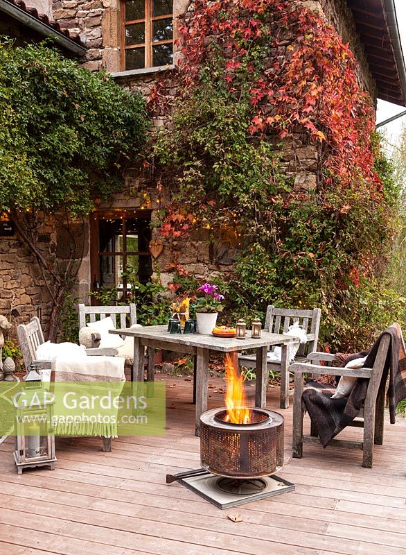 Garden table, chairs and fire basket on garden terrace set up for evening entertaining, Le Mas de BÃ©ty, France. 

