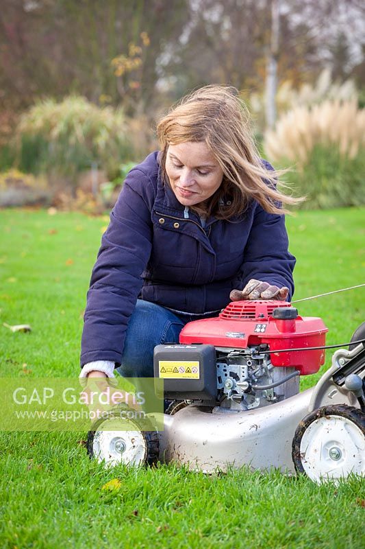 Raising the blades on a mower to adjust the cutting height before last cut of the year before winter