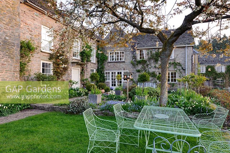 Wirework table and chairs on grass beside the terrace with cherry tree spreading overhead. Brilley Court Farm, Whitney-on-Wye, Herefordshire