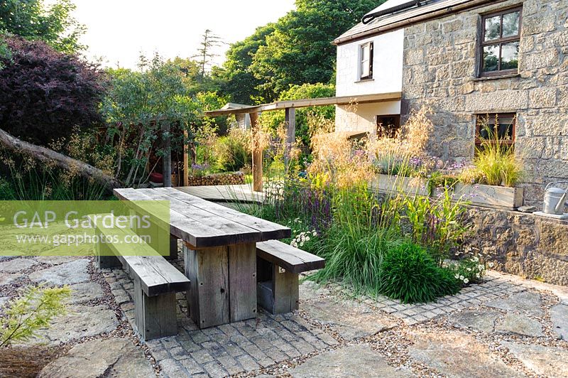 Chunky oak table and benches on a sunny terrace beside the house, Lower Treculliacks Farm, Falmouth, Cornwall, UK. 