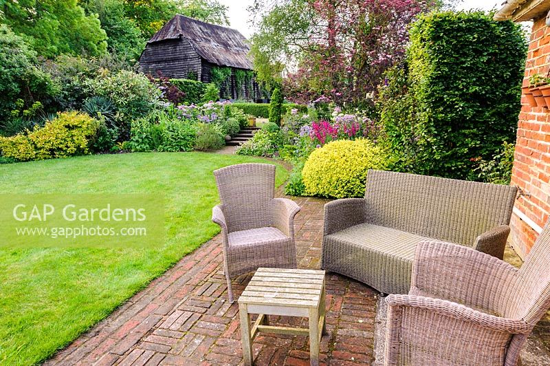 Seating area overlooking mixed colourful garden borders beyond, Terstan, Stockbridge, Hants, UK.