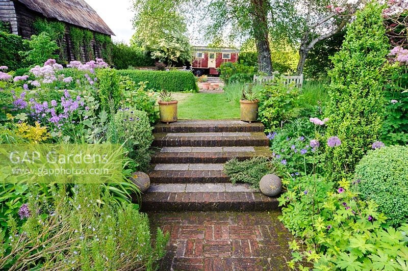 Brick steps lead between upper and lower garden, planted with beds planted with Buxus, hardy geraniums, Thalictrum aquilegiifolium, rosemary and alliums, Terstan, Stockbridge, Hants, UK. 

