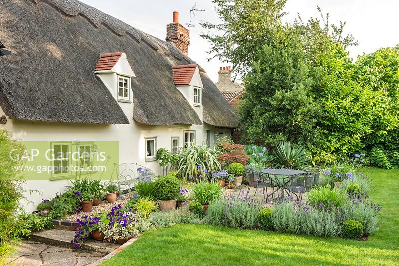 A view of a gravel garden, garden furniture and lawn of thatched cottage. 