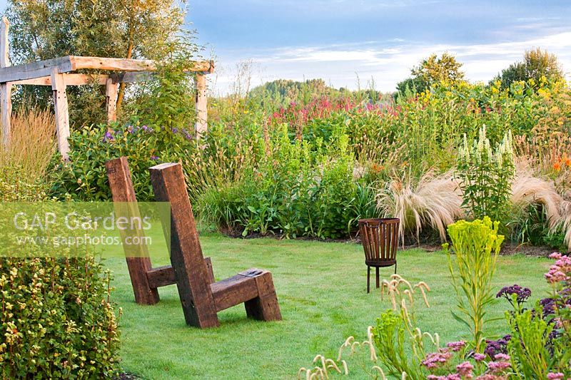Seats and fire basket surrounded with mixed borders of perennials and grasses in Frank Hejligens garden, Netherlands.