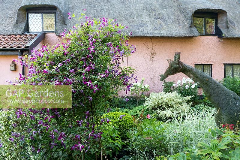 A giraffe wire mesh sculpture, made by Karen Roseberry, sits among shrubs in garden by cottage. 