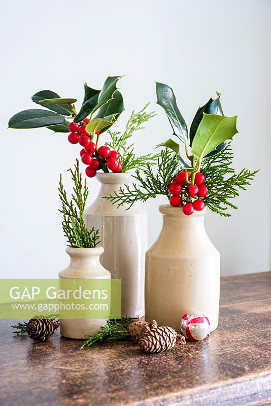 Cut Ilex with berries displayed in stoneware vases and dried winter accessories in home. 