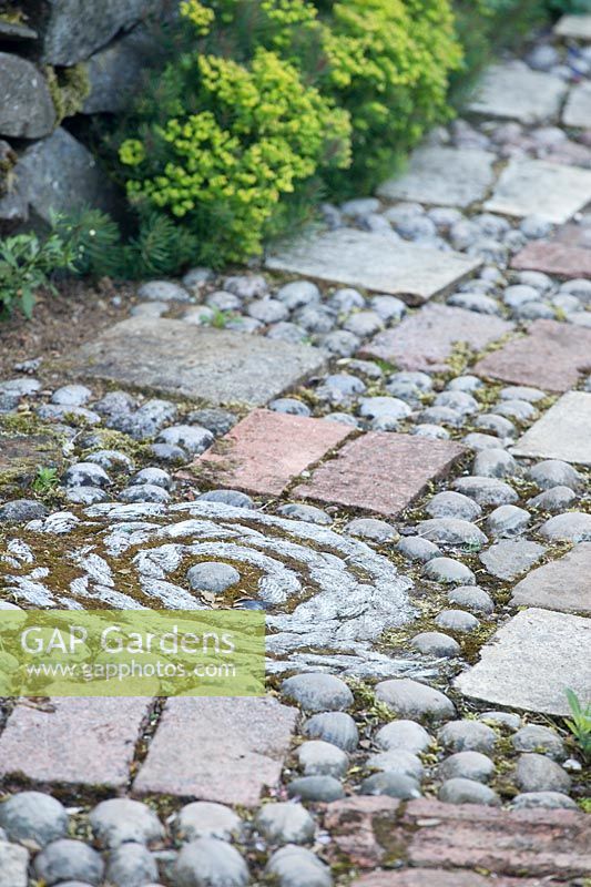 Close up of ornate path made with patterns of pebbles and paving slabs. 