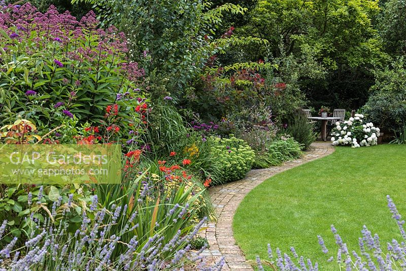 Packed herbaceous border with curved path leading to seating area. Plants include:
 of Lavandula - lavender, Eupatorium and Crocosmia
