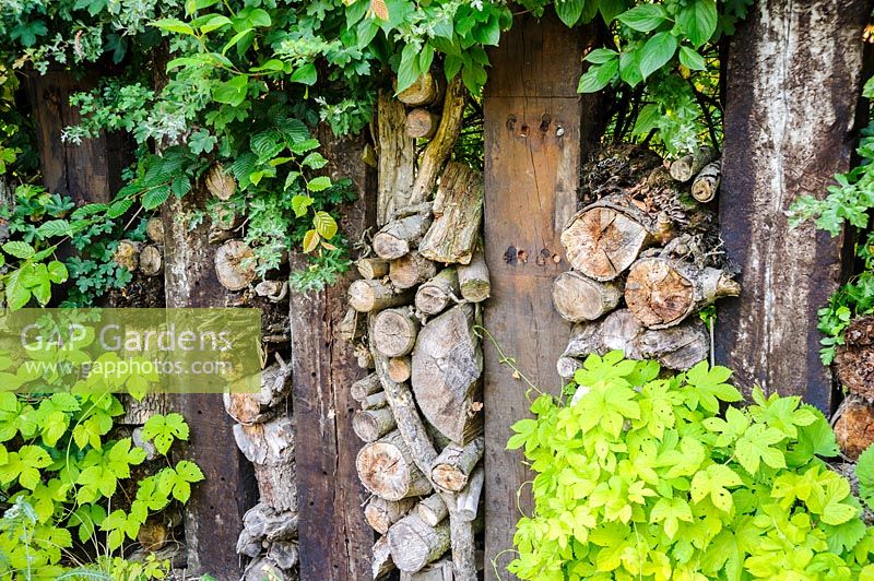 Garden featuring a boundary made using railway sleepers infilled with small logs, branches and twigs. Dipley Mill, Hartley Wintney, Hants, UK. 