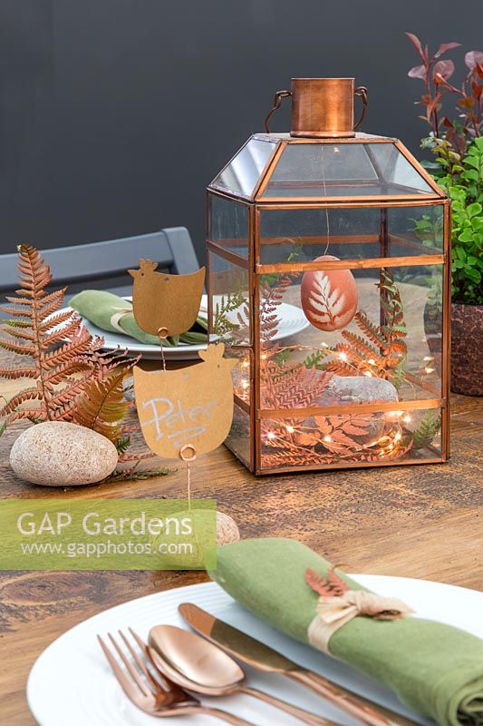 Copper themed Easter display in lantern with chicken shaped name cards fixed to pebbles with copper wire