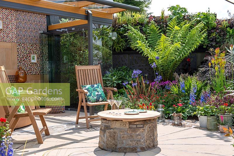 Wooden chairs and circular table in modern exotic garden. 'Jungle Fever', RHS Tatton Park Flower Show, 2018. 