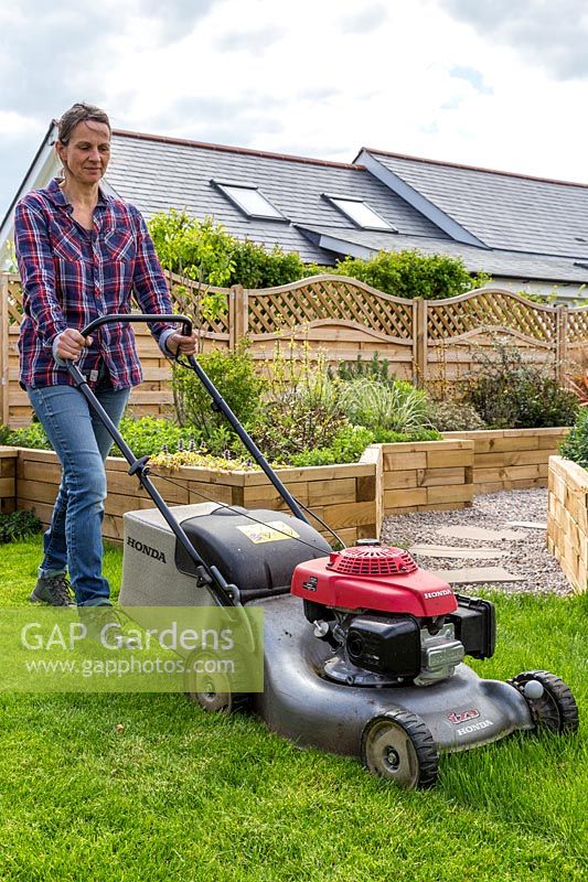 Woman mowing lawn with petrol lawn mower 