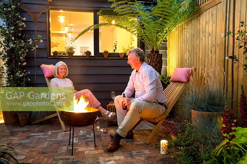 Garden owners Emma and Brian relaxing in garden next to their fire bowl. 
