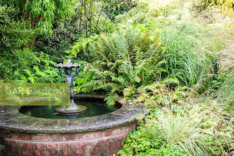 Circular pond with fountain and mixed foliage plants, ferns and bamboos - Shropshire, UK