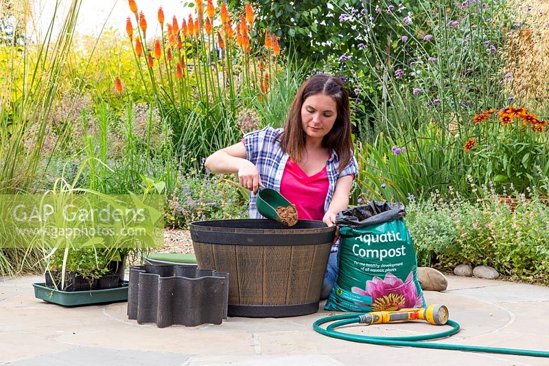 Woman adding aquatic compost to bottom of half barrel with scoop