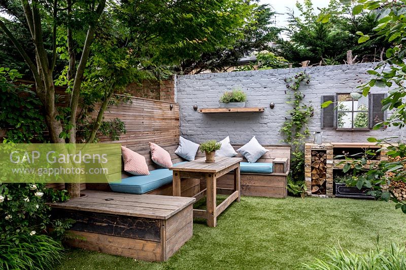 Small courtyard garden in West London with artificial lawn, built in Reclaimed 
Scaffold board seating and dining area with brick barbecue  
Garden designed by James Walsh.